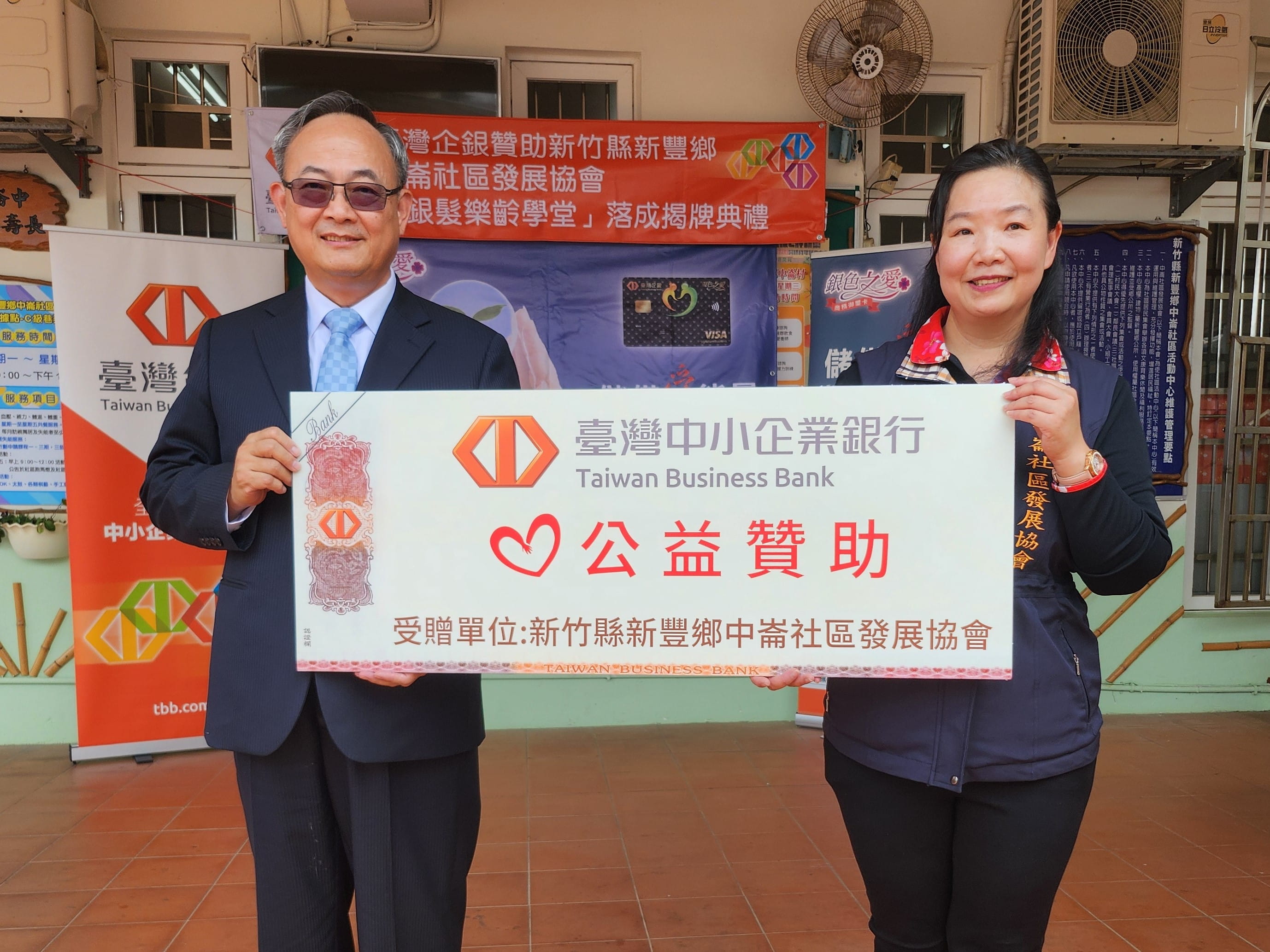 臺灣企銀銀髮樂齡學堂揭牌活動，由該行總經理張志堅（左）致贈公益支票予新竹縣新豐鄉中崙社區發展協會理事長郭玟伶。